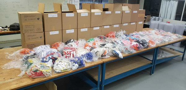 Dozens of bags of 3d printed face shield parts in a variety of colors lay across multiple tables waiting to be boxed up in Brazil.
