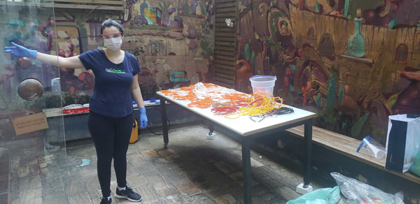 Female maker in Brazil sterilizes 3d printed face shield parts outside in a courtyard with murals.